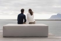 Vue arrière du couple assis sur pouf au bord du lac et regardant la vue — Photo de stock