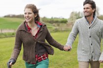 Happy couple holding hands while walking in field — Stock Photo