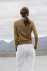 Vista trasera de la joven mujer de pie en la orilla del lago y mirando a la vista - foto de stock