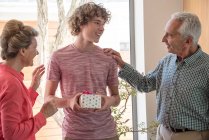 Glückliche Großeltern und Teenager-Enkel mit Geburtstagsgeschenk zu Hause — Stockfoto
