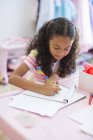 Целенаправленная маленькая девочка делает домашнее задание за розовым столом — стоковое фото