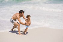 Homem alegre brincando com o filho na praia de areia — Fotografia de Stock