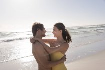 Sorrindo jovem casal abraçando na praia ensolarada — Fotografia de Stock
