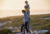 Jovem família feliz andando na praia ao pôr do sol — Fotografia de Stock