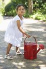 Симпатична маленька дівчинка в білому літньому платті, що тримає поливну банку в саду — стокове фото