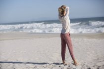 Mujer rubia relajada de pie en la playa soleada - foto de stock
