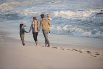 Vista trasera de la familia caminando arenoso en la playa - foto de stock