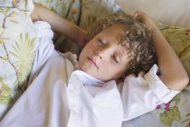 Niño con los ojos cerrados relajándose en el sofá - foto de stock