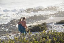 Romantisches Paar spaziert an der Küste mit Vegetation im Sonnenlicht — Stockfoto