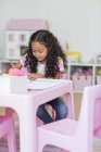 Маленька дівчинка робить домашнє завдання за рожевим столом у кімнаті — стокове фото