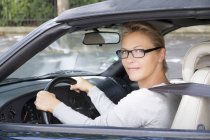 Primer plano de la mujer sonriente con anteojos que conducen un coche - foto de stock