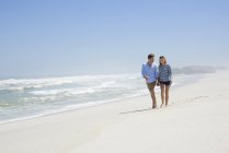 Happy couple walking on sandy beach holding hands — Stock Photo