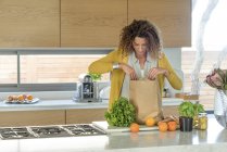 Woman taking out food from paper bag in kitchen — Stock Photo