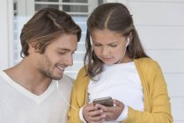 Счастливый отец с маленькой дочкой слушают музыку в наушниках мобильного телефона — стоковое фото