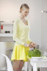 Junge elegante Frau mixt Salat am Esstisch — Stockfoto
