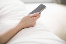 Крупный план женской руки, держащей мобильный телефон на кровати — стоковое фото