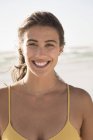 Lächelnde junge Frau blickt am Strand in die Kamera — Stockfoto