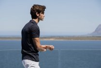 Юнак стоячи на балконі на відкритому повітрі з видом на море — стокове фото