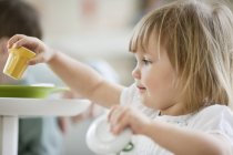 Милая маленькая девочка играет с игрушечным чайным сервизом за обеденным столом — стоковое фото