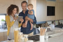 Pareja usando tableta digital con hija bebé en la cocina - foto de stock
