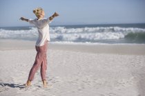 Relaxado jovem mulher com braço estendido em pé na praia ensolarada — Fotografia de Stock