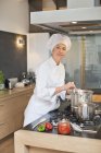 Frau im Kochkostüm kocht Essen in der Küche — Stockfoto