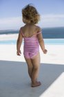 Primer plano de la niña en traje de baño rosa caminando cerca de la piscina - foto de stock