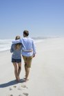 Вид сзади на романтическую пару, гуляющую по песчаному пляжу — стоковое фото