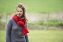 Jeune femme avec écharpe rouge marchant dans le champ — Photo de stock