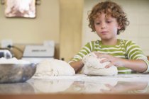 Cute little boy kneading dough in kitchen — Stock Photo