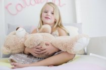 Portrait of cute little girl holding teddy bear on bed — Stock Photo