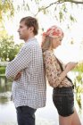 Side view of couple standing back to back with mobile phone — Stock Photo