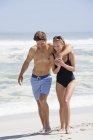 Couple riant en maillot de bain marchant sur la plage de sable — Photo de stock