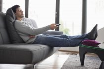 Mann liegt auf Couch und wechselt Kanäle mit Fernbedienung — Stockfoto