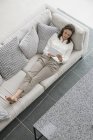 Donna sdraiata sul divano a casa e utilizzando tablet digitale — Foto stock