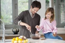 Man stirring mixture in bowl with daughter in kitchen — Stock Photo