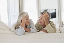 Portrait of smiling senior couple resting on bed at home and looking at each other — Stock Photo