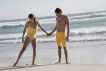 Счастливая пара в жёлтых купальниках и шортах, стоящих на песчаном пляже — стоковое фото