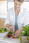 Mulher sênior feliz cortando legumes na cozinha — Fotografia de Stock