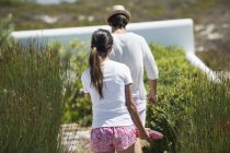 Blick von hinten auf junges Paar, das in sonnigem Garten spaziert — Stockfoto