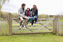 Boy sitting with parents on wooden fence in countryside — Stock Photo
