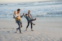 Familia feliz divirtiéndose en la playa al atardecer - foto de stock