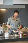 Mann bereitet Essen in Küche zu und schaut in Kamera — Stockfoto