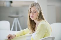 Serious young blonde woman sitting in room and looking away — Stock Photo