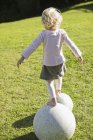 Вид сзади на маленькую девочку, идущую по каменной сфере на зеленой лужайке — стоковое фото