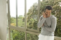 Sorrindo homem telefonando enquanto se inclina na janela no jardim — Fotografia de Stock