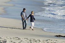 Couple holding hands, walking on sandy beach — Stock Photo