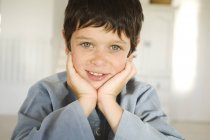 Kleiner sommersprossiger Junge lächelt und blickt in die Kamera am Holztisch — Stockfoto