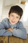 Kleiner sommersprossiger Junge lächelt und blickt in die Kamera am Holztisch — Stockfoto