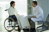 Medico di sesso maschile che parla con paziente donna in sedia a rotelle in ospedale — Foto stock